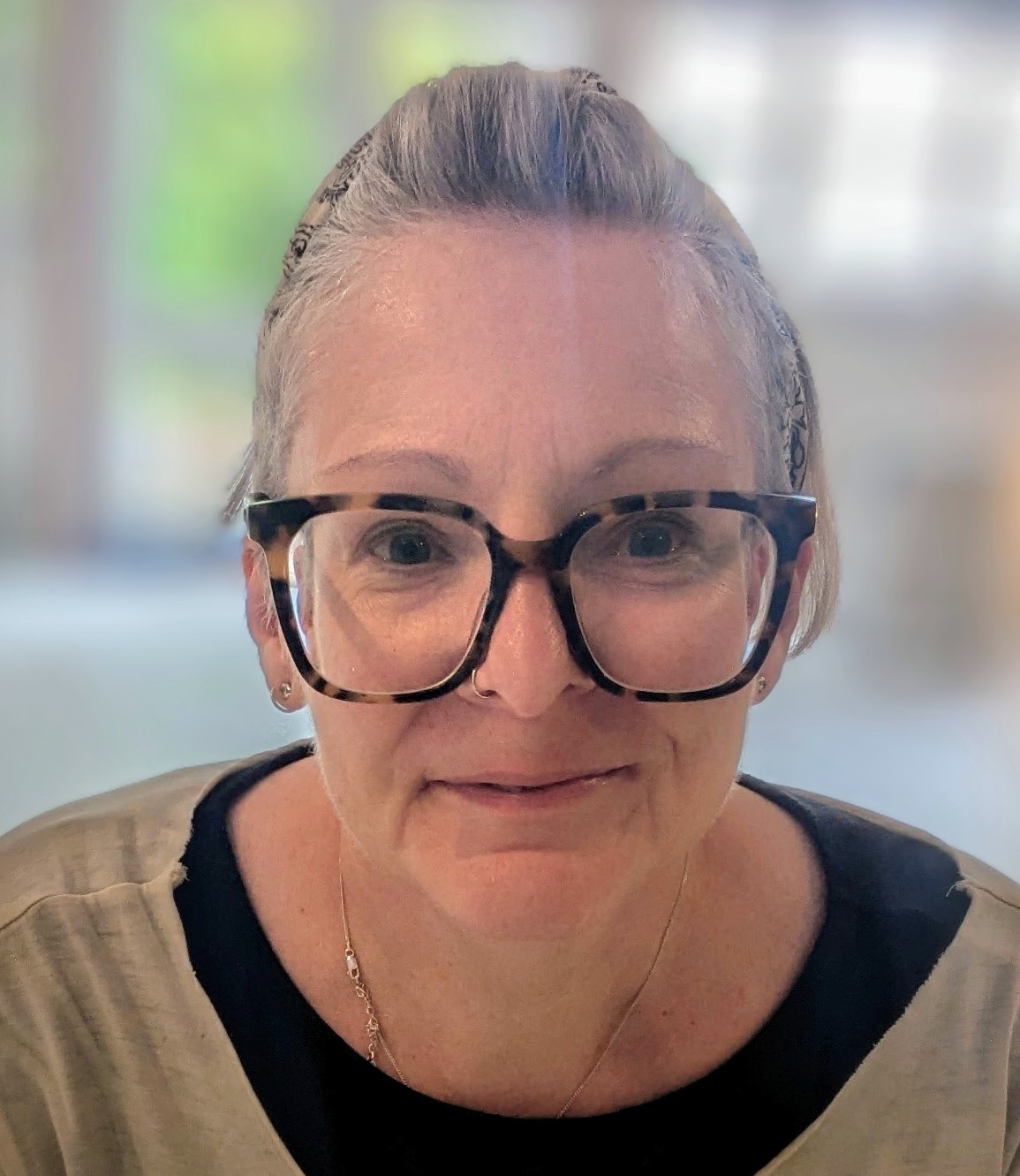Headshot photo of Jude Mills.   Female presenting preson waring large glasses and smiling.
